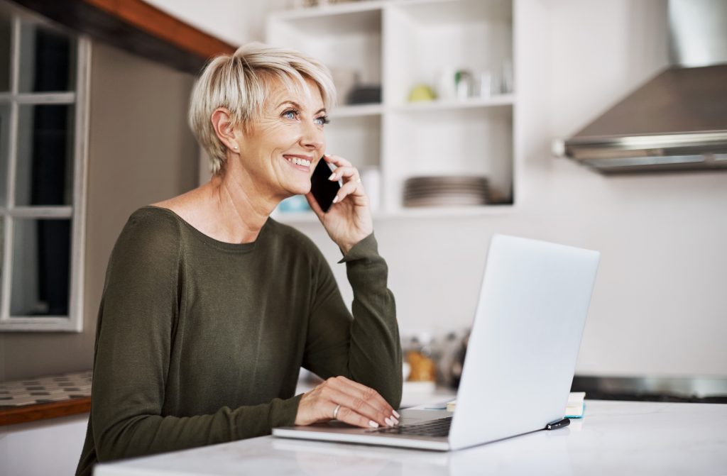 Shot of a mature woman talking on a cellphone while using a laptop at home