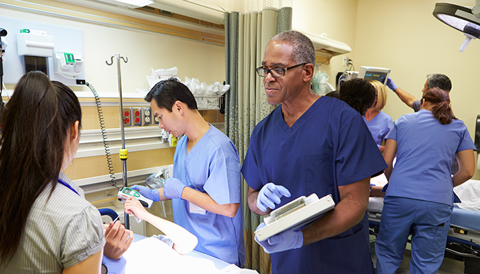 Hands holding defibrillator paddles over a patient’s chest, ready to deliver an electric shock in an emergency room setting.
