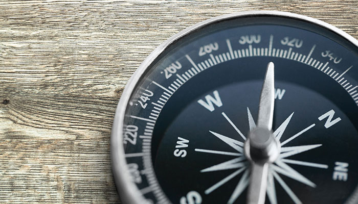 A close-up photograph of a brass or vintage compass resting on a weathered wooden background, symbolizing direction, guidance, and navigation.