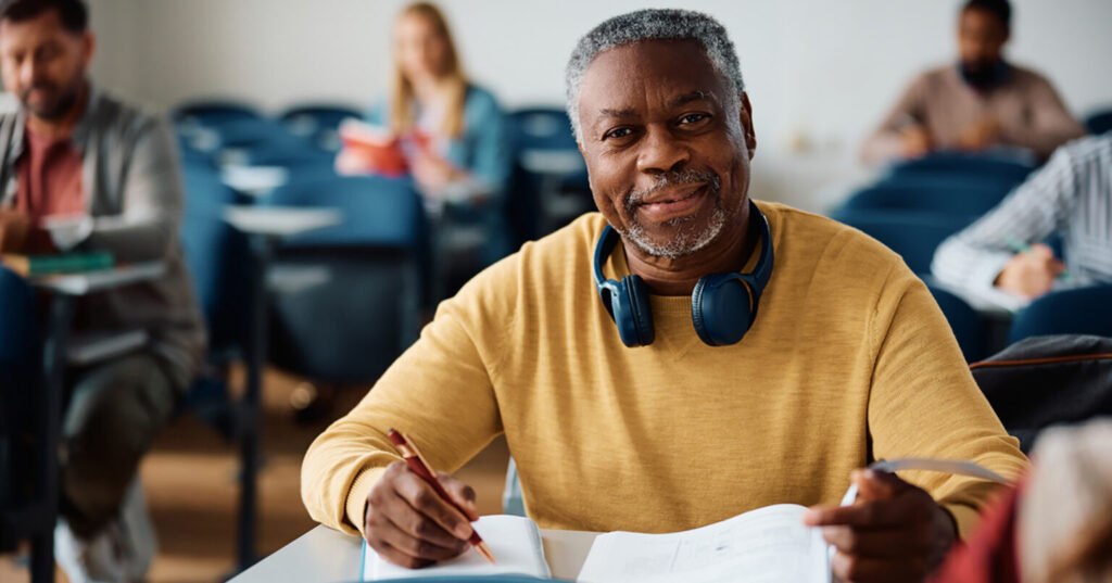 Smiling black senior man learning during adult education course and looking at camera.